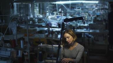 年轻女子制衣工人是在夜班期间在一家服装厂缝纫而灯都关掉在背景中.